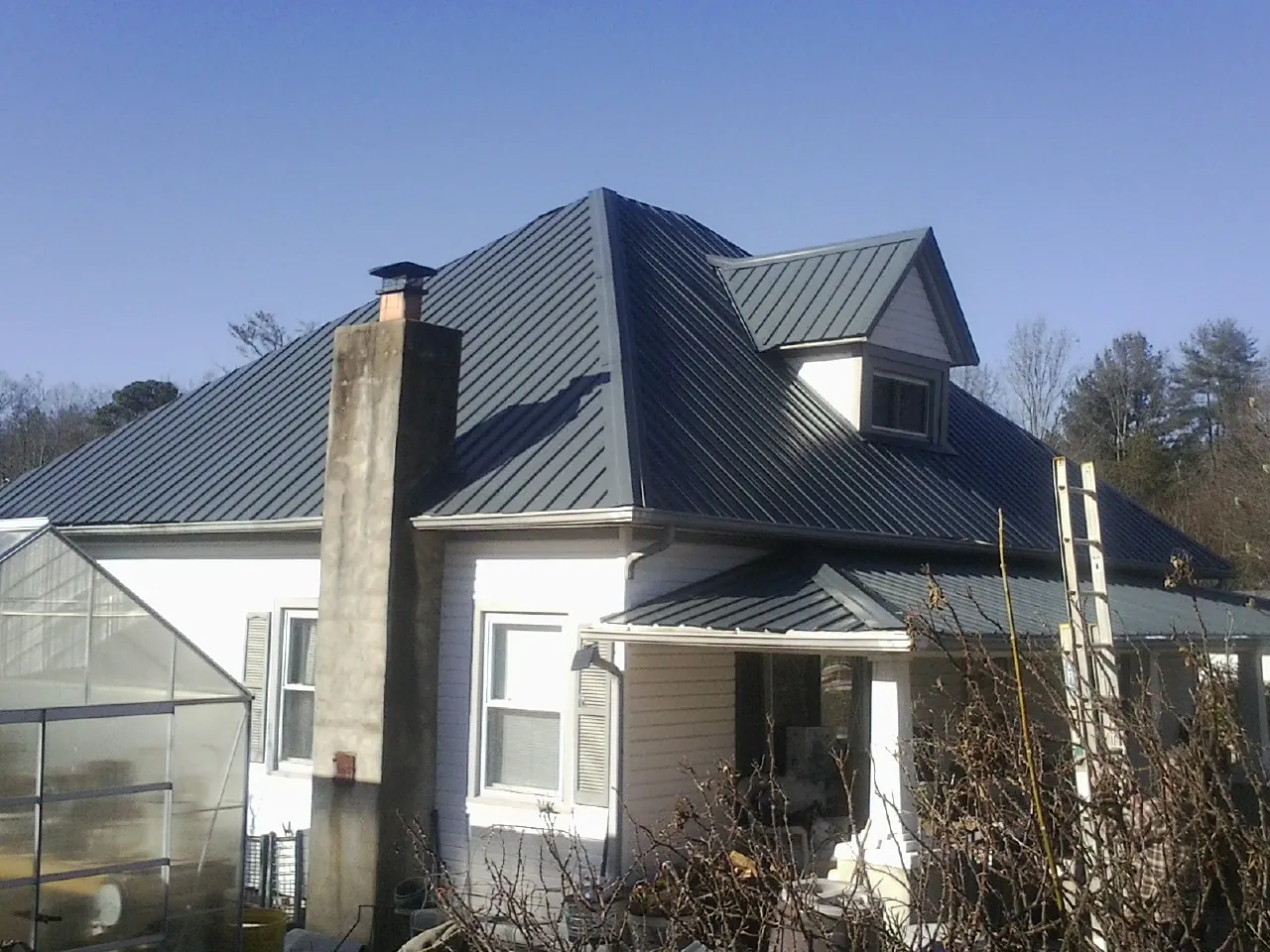 Dark blue standing seam metal roof on a white farmhouse with dormer — Slate & Tile Roof Repair by Roofing Brothers in Glenfield