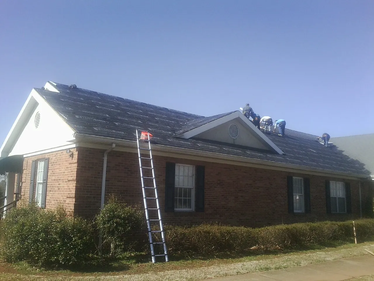 Crew tearing shingles off a brick ranch roof with a ladder set — Metal Roof Repair work by our crew in Glenfield