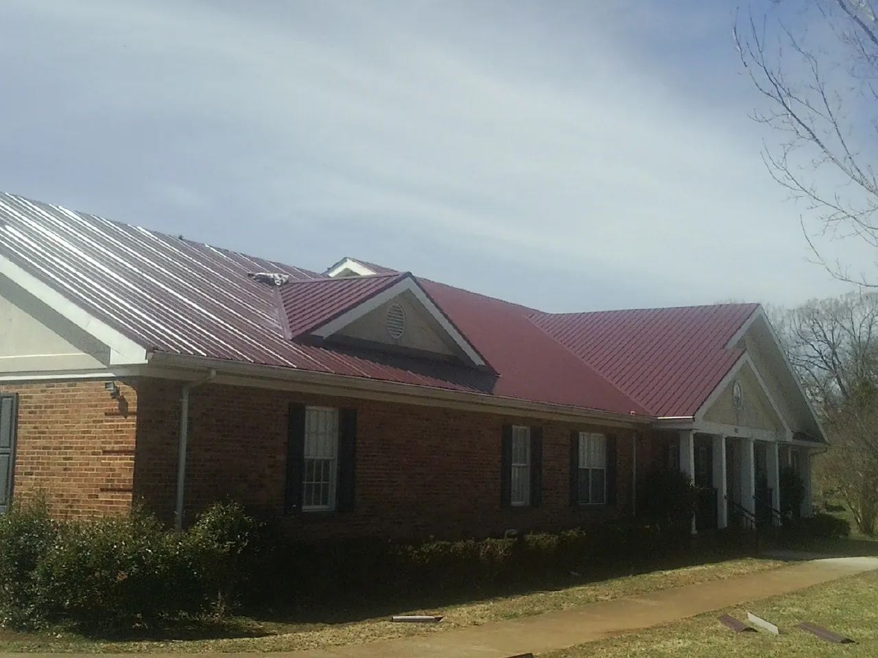 Red metal roof with gabled entries on a long brick building, from a Hail Damage Roof Repair job in Glenfield