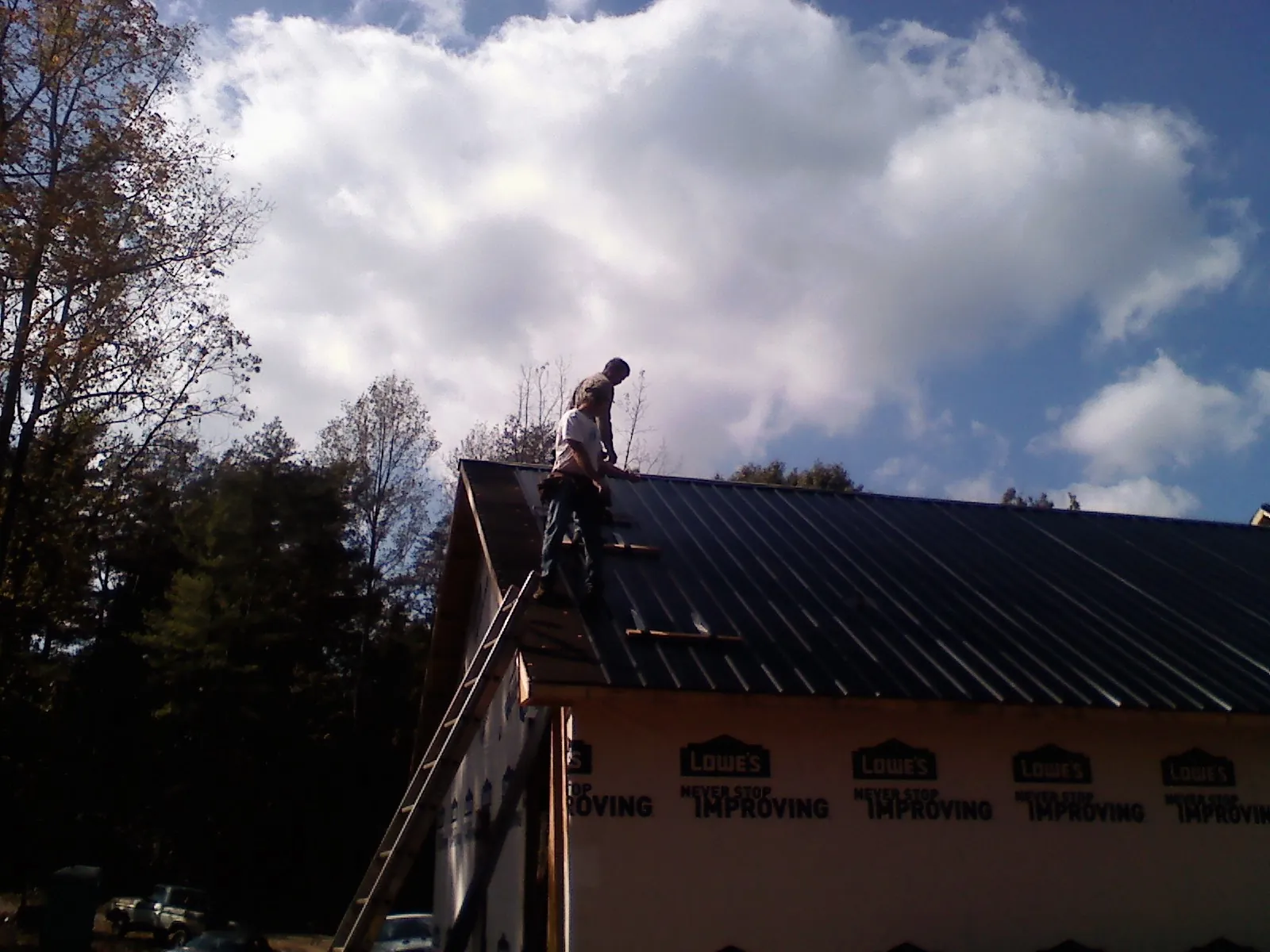 Roofer fastening dark metal panels high against a cloudy sky, from a Roof Inspection job in Glenfield