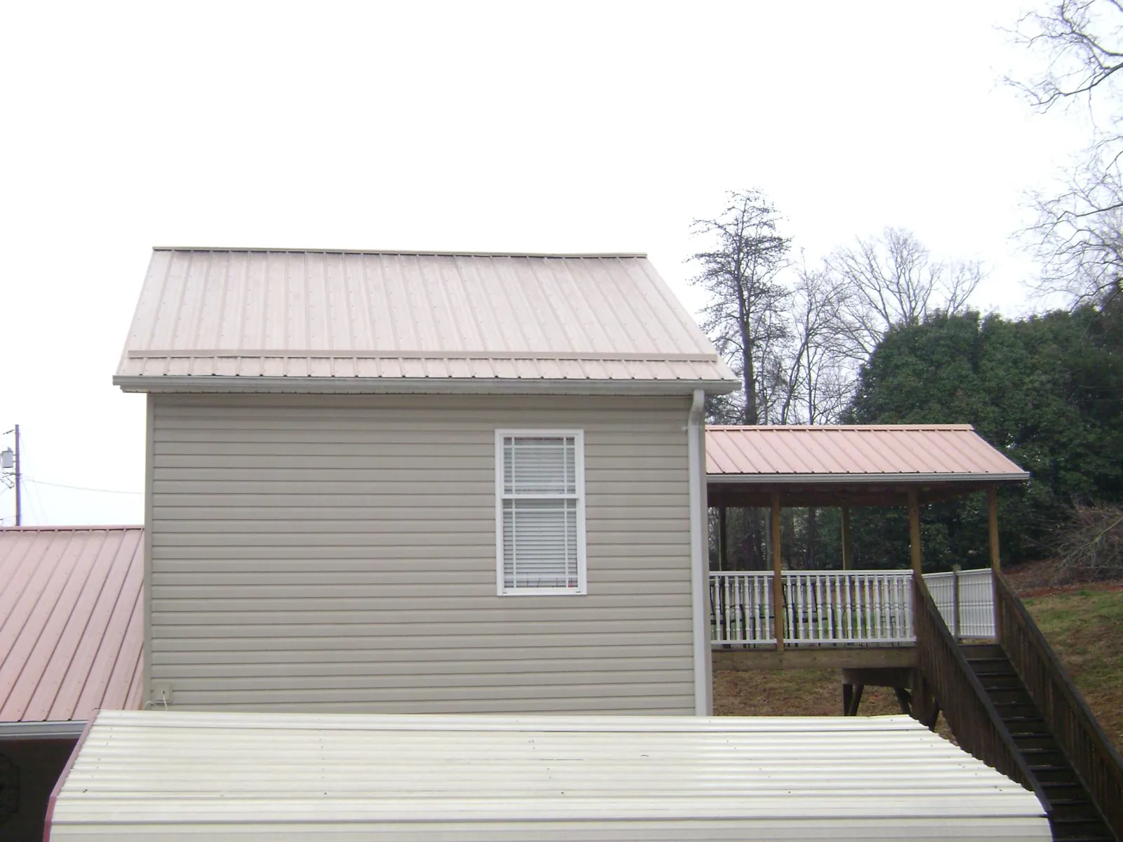 Tan metal roofs on a two story addition and attached porch, from a Roof Replacement job in Glenfield